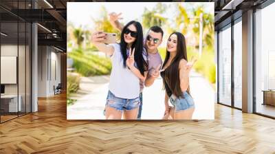 Three young friends, man is taking a self-portrait with two girls are enjoying their summer vacation. Wall mural